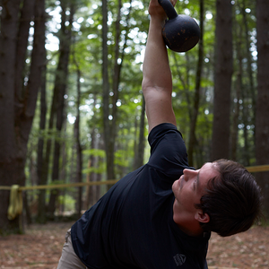 Strong young man holding dumbbell with trees in background