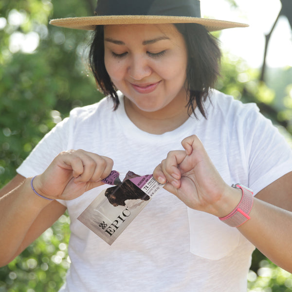 A woman outside opening EPIC's Grass-fed Bison Bacon Cranberry Bar.