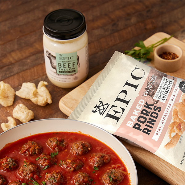 EPIC Provisions' Pink Himalayan Sea Salt Baked Rinds in brand new packaging laying on a cutting board next to a sauté' pan of meatballs and a jar of EPIC Provisions' Beef Tallow.
