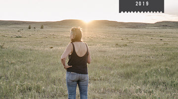 A woman stands in front of a pasture where the sun is setting.