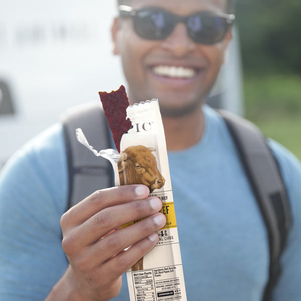 A man wearing sunglasses holding an open EPIC Grass-fed Wagyu Beef Snack Strip showing the camera.