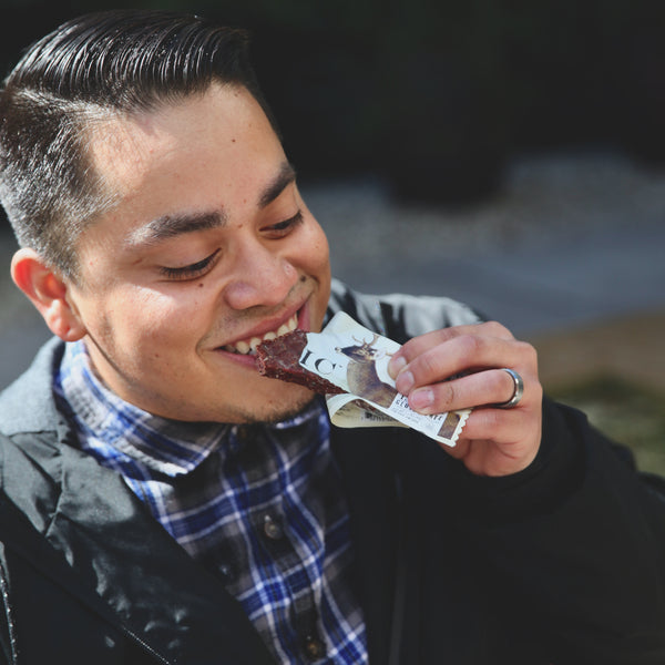 A man eating a bit of an EPIC Grass-fed Vension Sea Salt Pepper Bar outside.